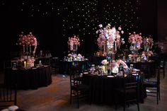 a room filled with tables covered in black cloths and tall vases full of flowers