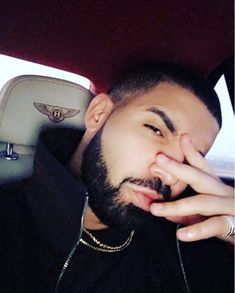 a man with a beard sitting in the back seat of a car and holding his hand to his face