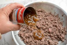 a person pouring sauce into a bowl filled with ground beef and other ingredients to make hamburger patties