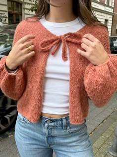 a woman is wearing an orange cardigan with a bow at the neck and jeans