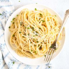 a white plate topped with pasta and parmesan cheese next to a silver fork