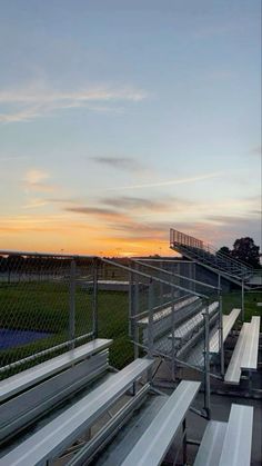 the sun is setting over an empty baseball field with white benches and bleachers