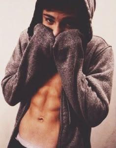 a shirtless young man covers his face with his hands while wearing a hoodie