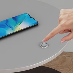 a woman's hand is pointing at an electronic device on a round table with a phone in the background