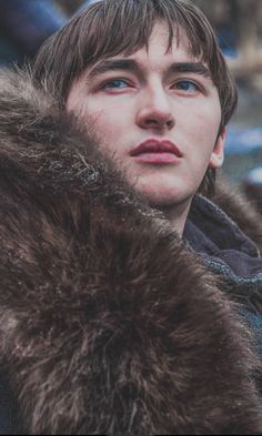 a young man with blue eyes wearing a fur coat and looking off to the side