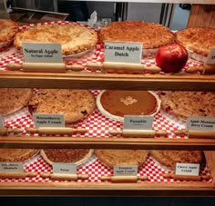 several different types of pies on display in a bakery case with red and white checkered paper