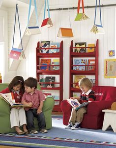 three children sitting on chairs reading books in a room with red bookcases and blue carpet