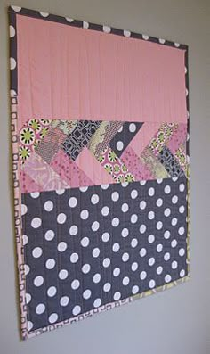 a pink and black wall hanging with polka dots on the bottom, along with a patchwork design