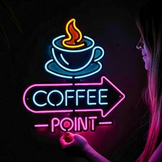 a woman holding a neon sign that says coffee point with a cup on it in front of her