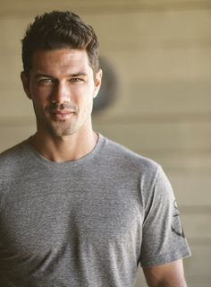 a man in a gray shirt is posing for a photo with his hands in his pockets