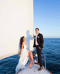 a man and woman standing on the deck of a sailboat posing for a photo