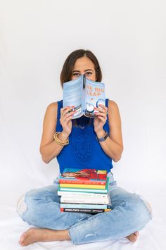 a woman is sitting on the floor and reading a book with her eyes closed while holding several books in front of her face