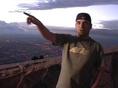 a man standing on top of a cliff pointing to the sky