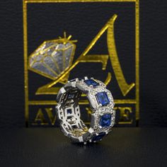 a diamond and blue sapphire ring sitting on top of a black table next to a golden logo