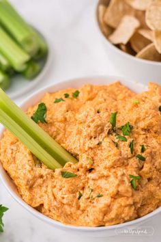 celery sticks sticking out of a dip in a white bowl next to chips