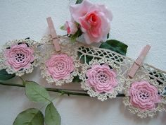 pink crocheted flowers and clothes pins are on a white surface next to a rose