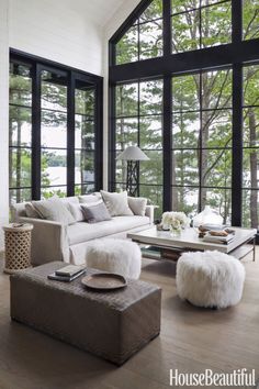 a living room filled with lots of windows next to a white couch and ottomans