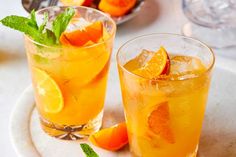 two glasses filled with orange juice and garnished with mint on a white plate