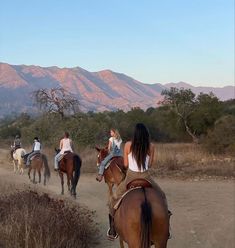 four people are riding horses on a dirt path in front of some hills and trees