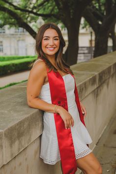 a woman wearing a red and white dress leaning against a wall with trees in the background