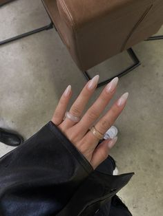 a woman's hand with white and beige manicures on it, sitting in front of a brown chair