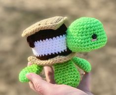 a hand holding a small crocheted turtle with a hat on it's head