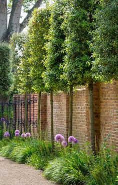 a brick fence with trees and flowers along it