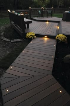 a wooden deck with lights on it and some flowers in the grass next to it