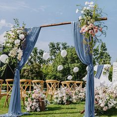 an outdoor wedding setup with blue drapes and white flowers on the grass, balloons in the air