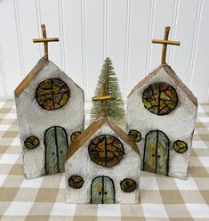 three small white houses with stained glass windows and crosses on the roof, sitting on a checkered tablecloth