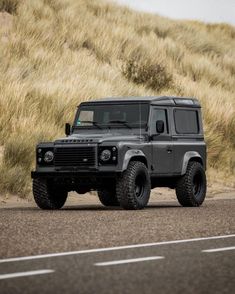 a grey land rover is parked on the side of the road in front of a grassy hill