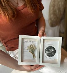 the woman is holding two framed pictures with flowers in them, and one has her hand on