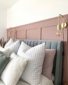 a bed topped with lots of pillows next to a pink headboard and light fixture