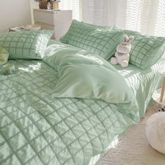 a teddy bear sitting on top of a green comforter in a room with white curtains