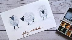 a card with three sheep on it next to some watercolor paints