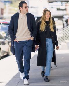 a man and woman are walking down the street together, both wearing coats and jeans