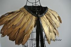 a black and gold dress with large feathers on it's chest, hanging from a wire rack