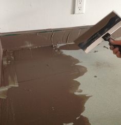 a person using a paint roller to apply brown paint on the floor in a room