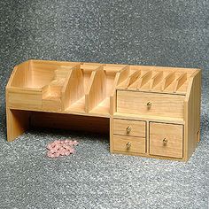 a toy wooden desk with drawers and pink flowers on the ground in front of it