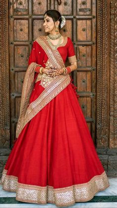 a woman in a red and gold bridal gown standing next to a wooden door