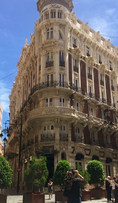 a tall building with many windows and balconies on the top floor, along with people walking around