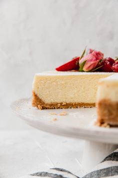 a slice of cheesecake on a white plate with strawberries and flowers in the background