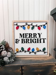 a merry and bright sign sitting on top of a wooden table next to pine cones