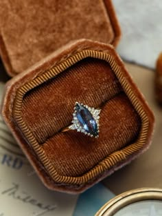 an engagement ring sits in a velvet box on top of some other jewelry and watches