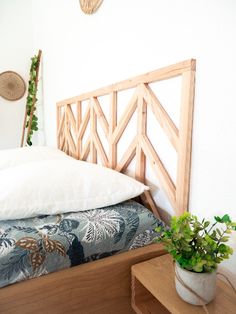 a bed with white pillows and wooden headboard next to a plant in a pot