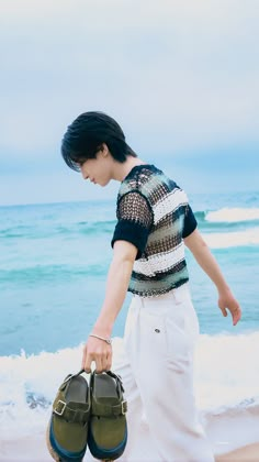 a young man walking on the beach holding two shoes