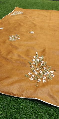 an orange blanket with white flowers on it sitting in the grass next to a tree