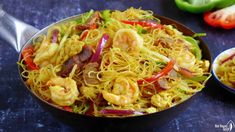 a bowl filled with noodles and shrimp on top of a blue counter next to peppers