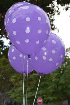 three purple balloons with white polka dots on them in front of a stop sign and trees