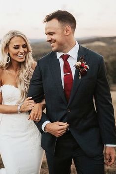 a bride and groom are walking together in the field at sunset or sunrise, with one holding his arm around the other's shoulder